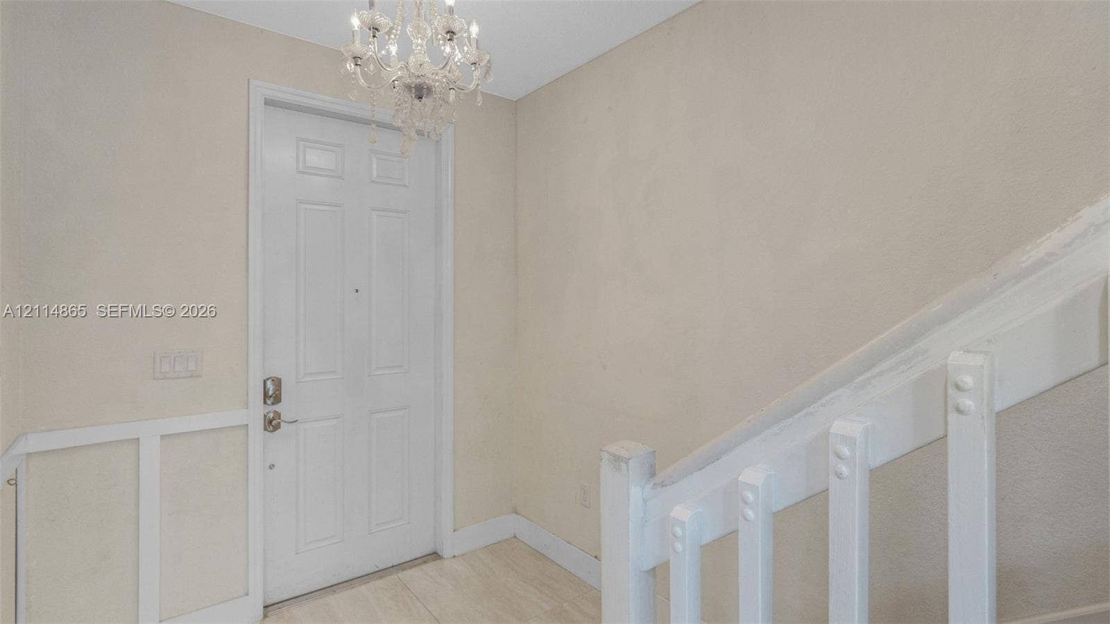 3754 NE 2nd Street, Homestead, FL 33033 Entryway featuring a white paneled door, crystal-style chandelier, light-toned flooring, and a white staircase with a wooden railing and vertical balusters