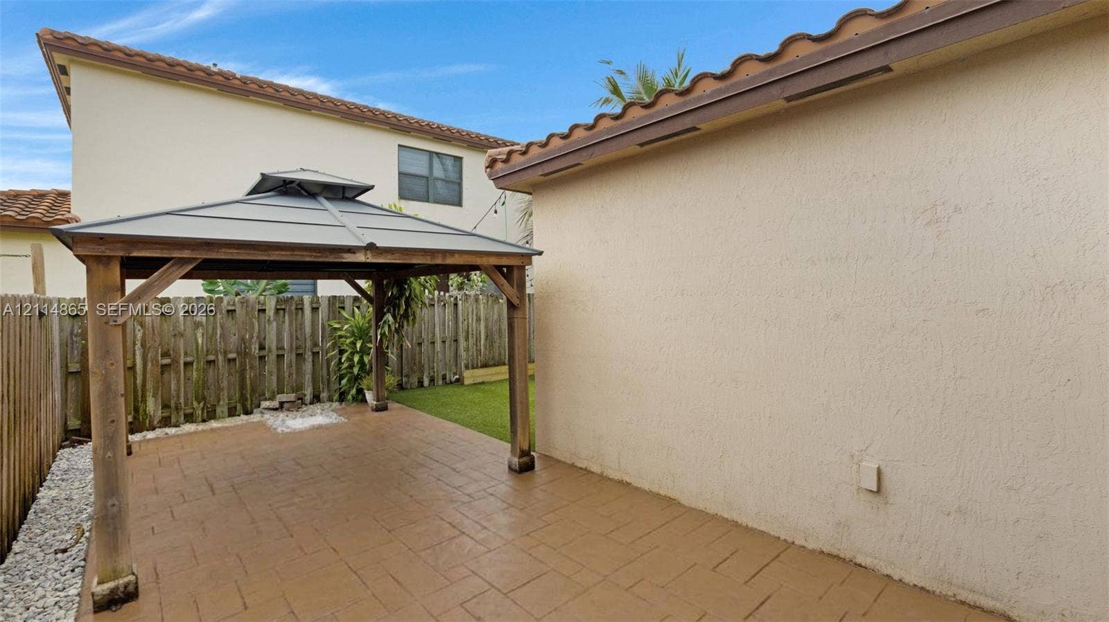 3754 NE 2nd Street, Homestead, FL 33033 Backyard featuring a covered patio with stamped concrete flooring, a wooden gazebo, a perimeter wood fence, and a synthetic turf area
