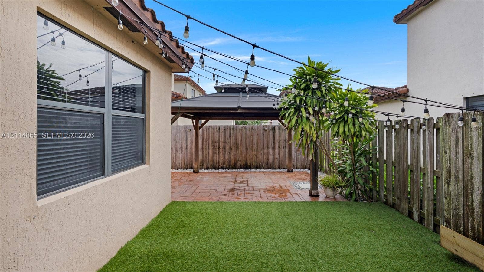 3754 NE 2nd Street, Homestead, FL 33033 Private backyard featuring artificial turf, a paved patio, a covered wooden gazebo, and perimeter wood fencing