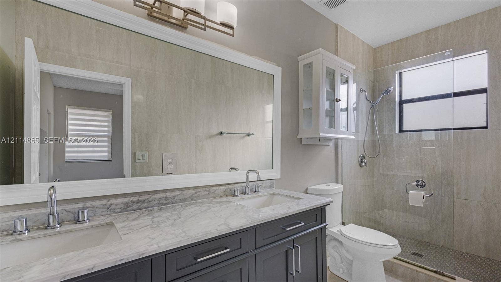 3754 NE 2nd Street, Homestead, FL 33033 Dual-sink vanity with stone countertop and cabinetry, large framed mirror, wall-mounted glass cabinetry, and walk-in shower with glass enclosure