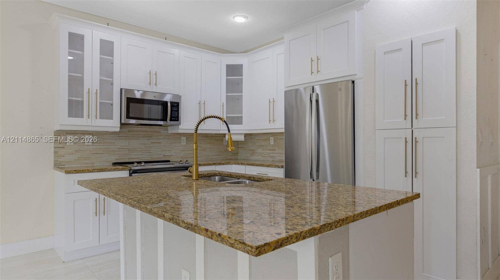 3754 NE 2nd Street, Homestead, FL 33033 Kitchen featuring white shaker-style cabinetry, stone countertops, stainless steel appliances, a center island, and a gold-tone faucet