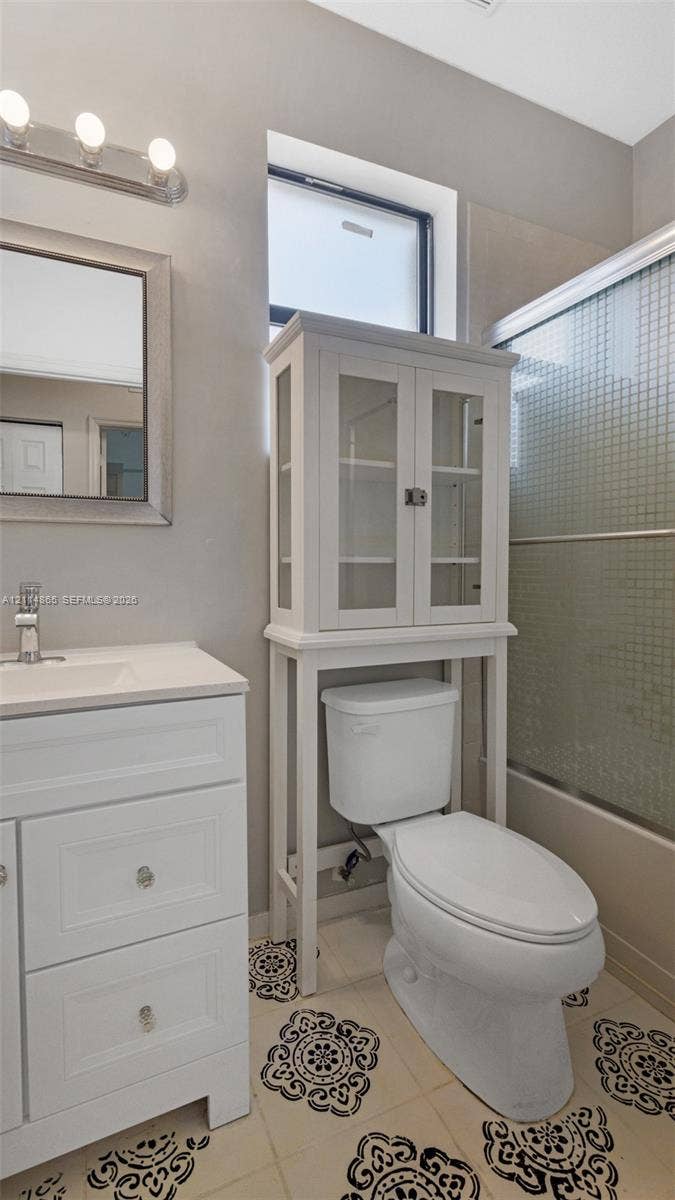 3754 NE 2nd Street, Homestead, FL 33033 2nd floor full Bathroom featuring white shaker-style cabinetry with a smooth surface countertop, patterned tile flooring, a multi-light wall fixture, and a glass-enclosed shower