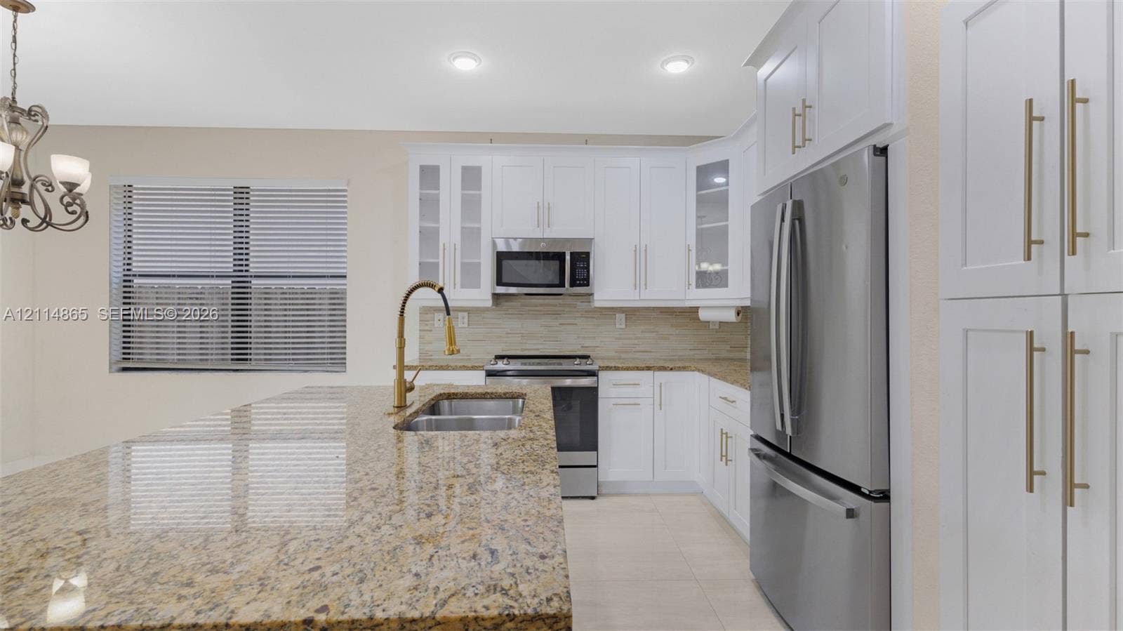 3754 NE 2nd Street, Homestead, FL 33033 Kitchen featuring white shaker-style cabinetry, stone countertops, a central island with an integrated double-basin sink and arched faucet, stainless steel appliances, and a tile backsplash
