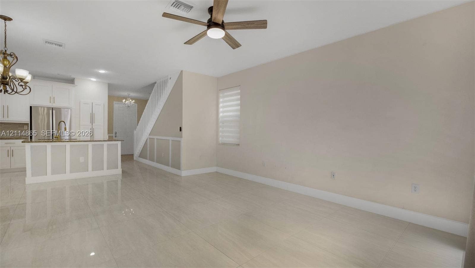 3754 NE 2nd Street, Homestead, FL 33033 Open living area featuring large-format polished tile flooring, neutral wall tones, beadboard wainscoting, multi-blade ceiling fan, and kitchen with white cabinetry and island