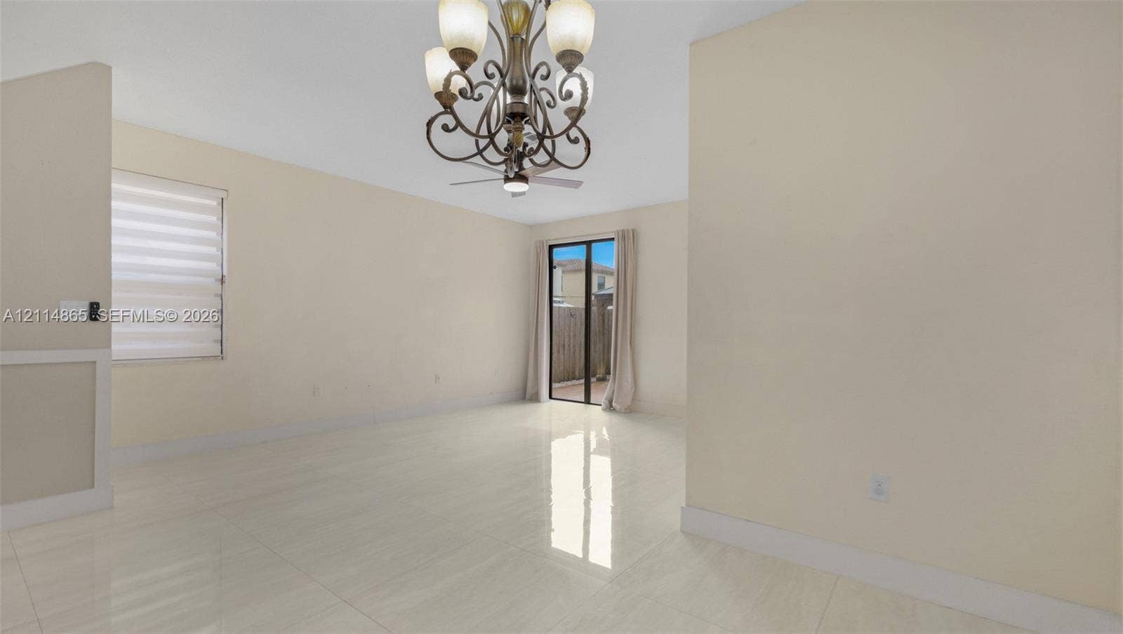 3754 NE 2nd Street, Homestead, FL 33033 Open-concept room featuring polished tile flooring, decorative multi-arm chandelier, ceiling fan, sliding glass door, and adjustable window blinds