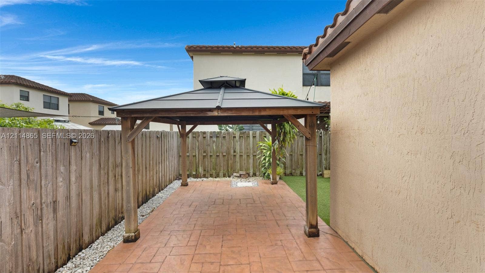 3754 NE 2nd Street, Homestead, FL 33033 Covered outdoor gazebo featuring a metal roof and wood-frame structure set upon a stamped concrete patio, enclosed by a wood privacy fence