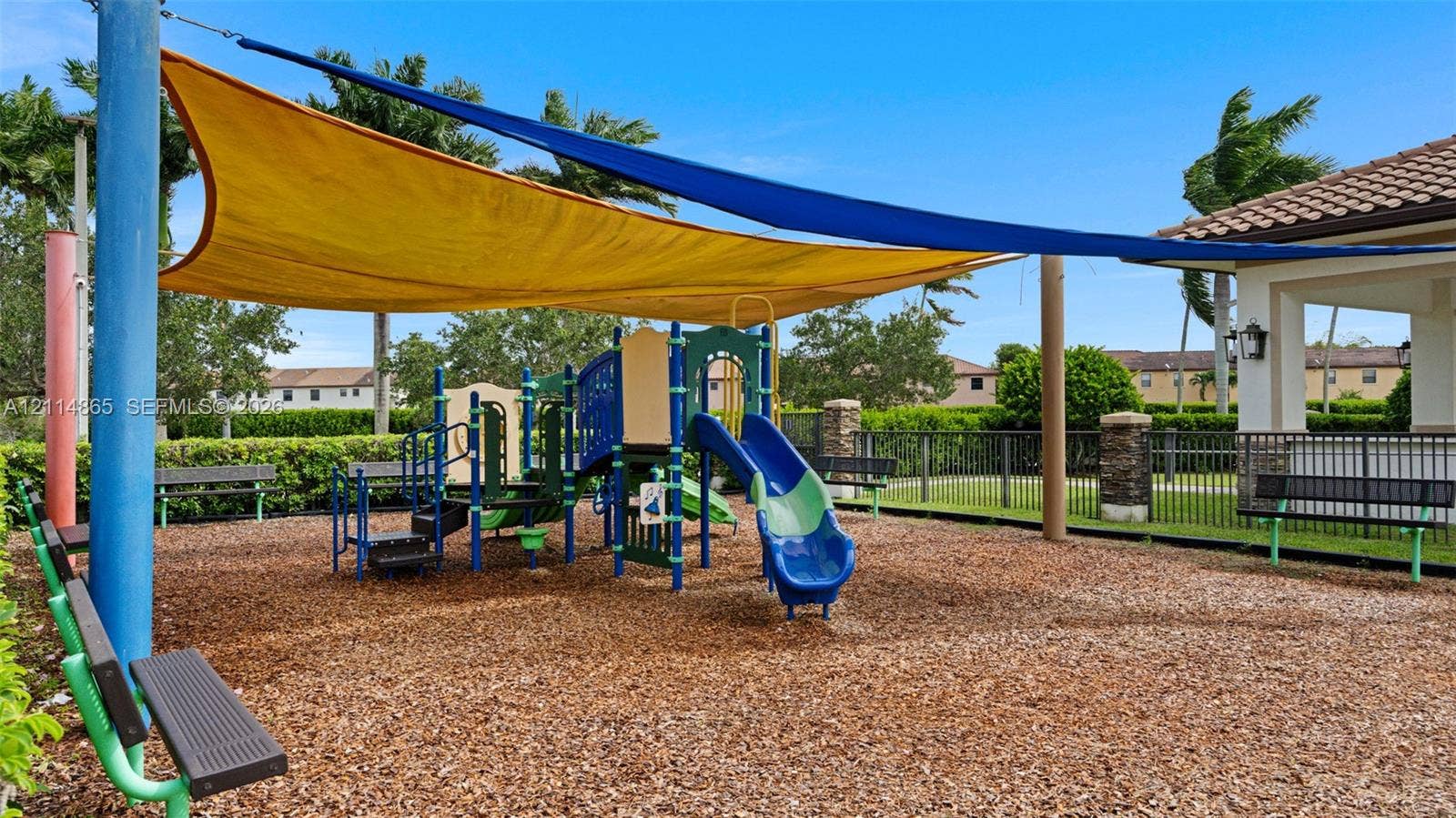 3754 NE 2nd Street, Homestead, FL 33033 Play area featuring multi-level climbing equipment, a blue slide, structural shade sails, and perimeter metal fencing