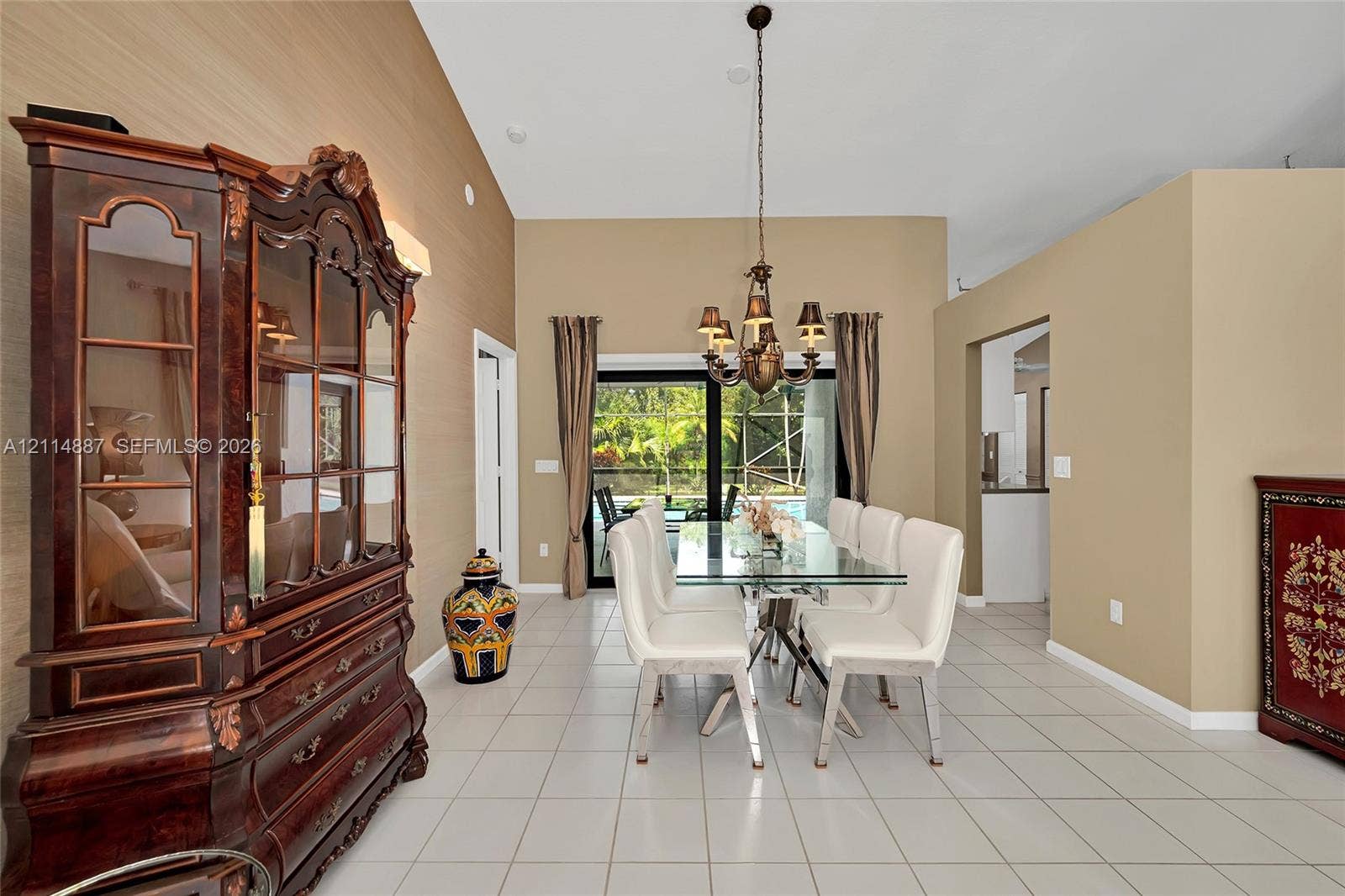 5722 Aspen Ridge Circle, Delray Beach, FL 33484 Vaulted ceilings, ceramic tile flooring, textured wall finishes, and a multi-arm metal chandelier, featuring sliding glass doors to a screened outdoor area
