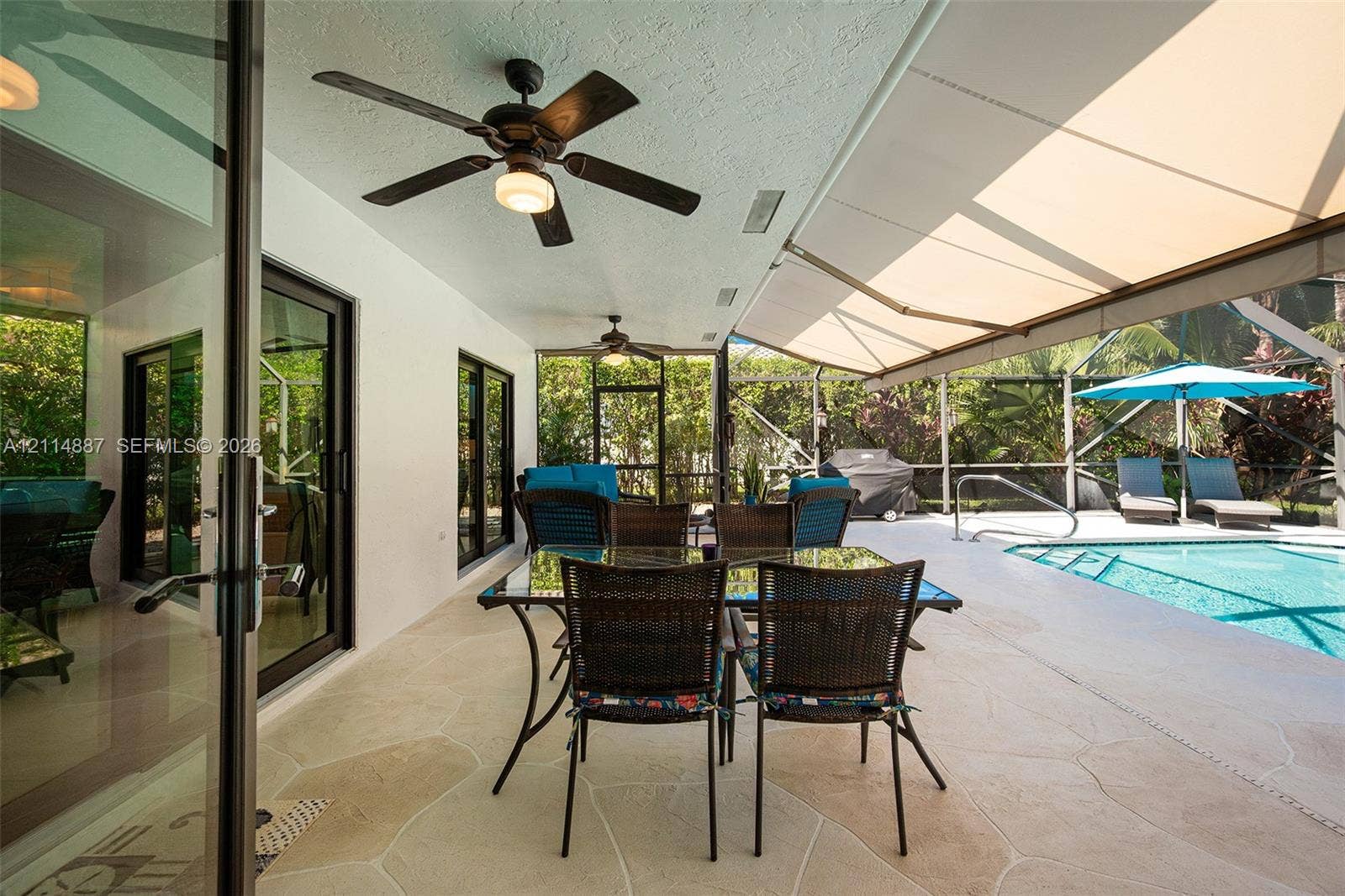 5722 Aspen Ridge Circle, Delray Beach, FL 33484 Covered screened-in lanai featuring stone-tile flooring, dual ceiling fans, a retractable fabric awning, and a built-in swimming pool