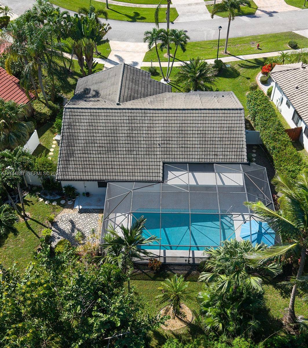 5722 Aspen Ridge Circle, Delray Beach, FL 33484 Tile roof structure featuring a screened-in swimming pool enclosure, paver patio, and landscaped perimeter with mature palm trees