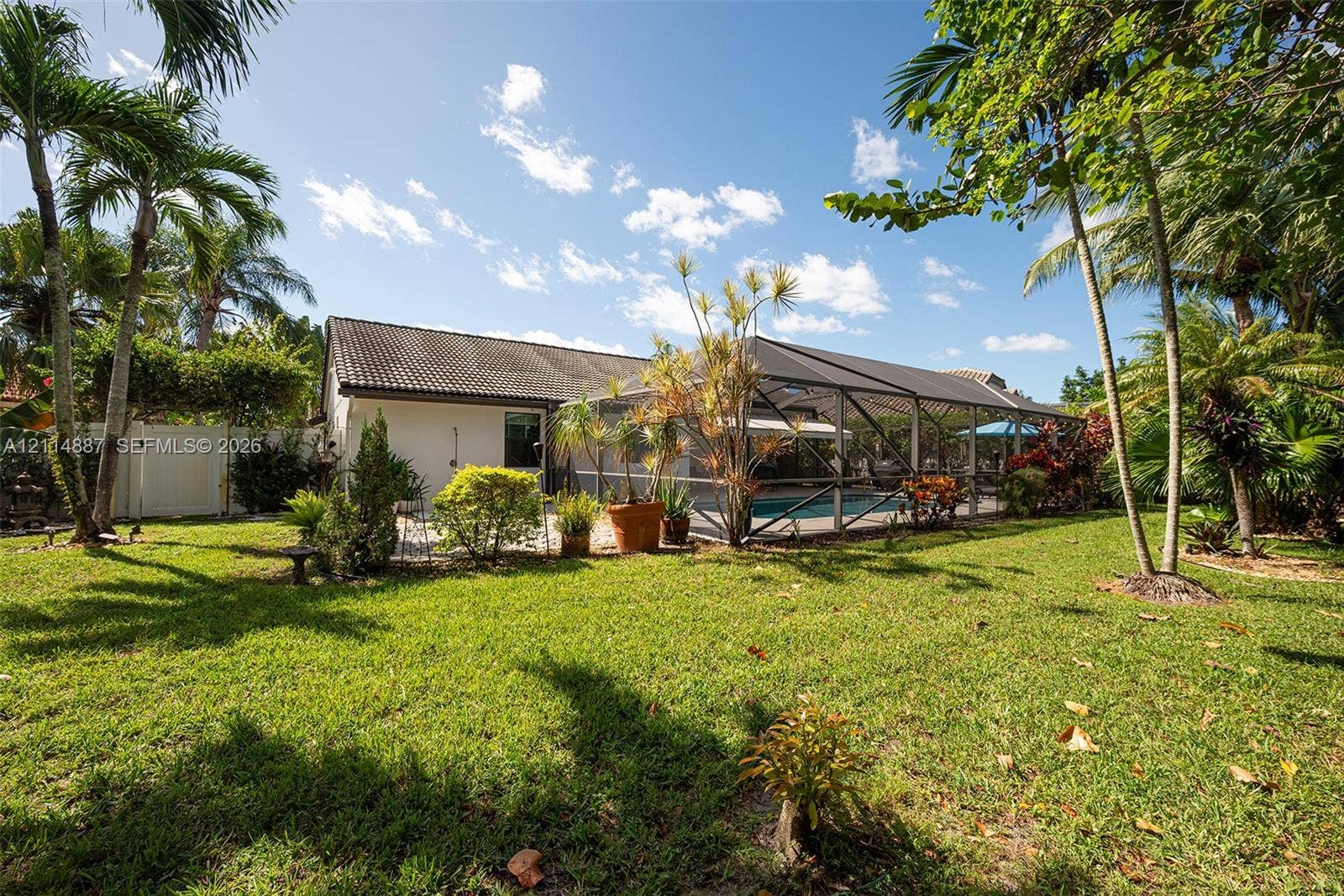 5722 Aspen Ridge Circle, Delray Beach, FL 33484 Spacious backyard featuring a manicured lawn, perimeter vinyl fencing, mature palm trees, and an enclosed screened-in pool area