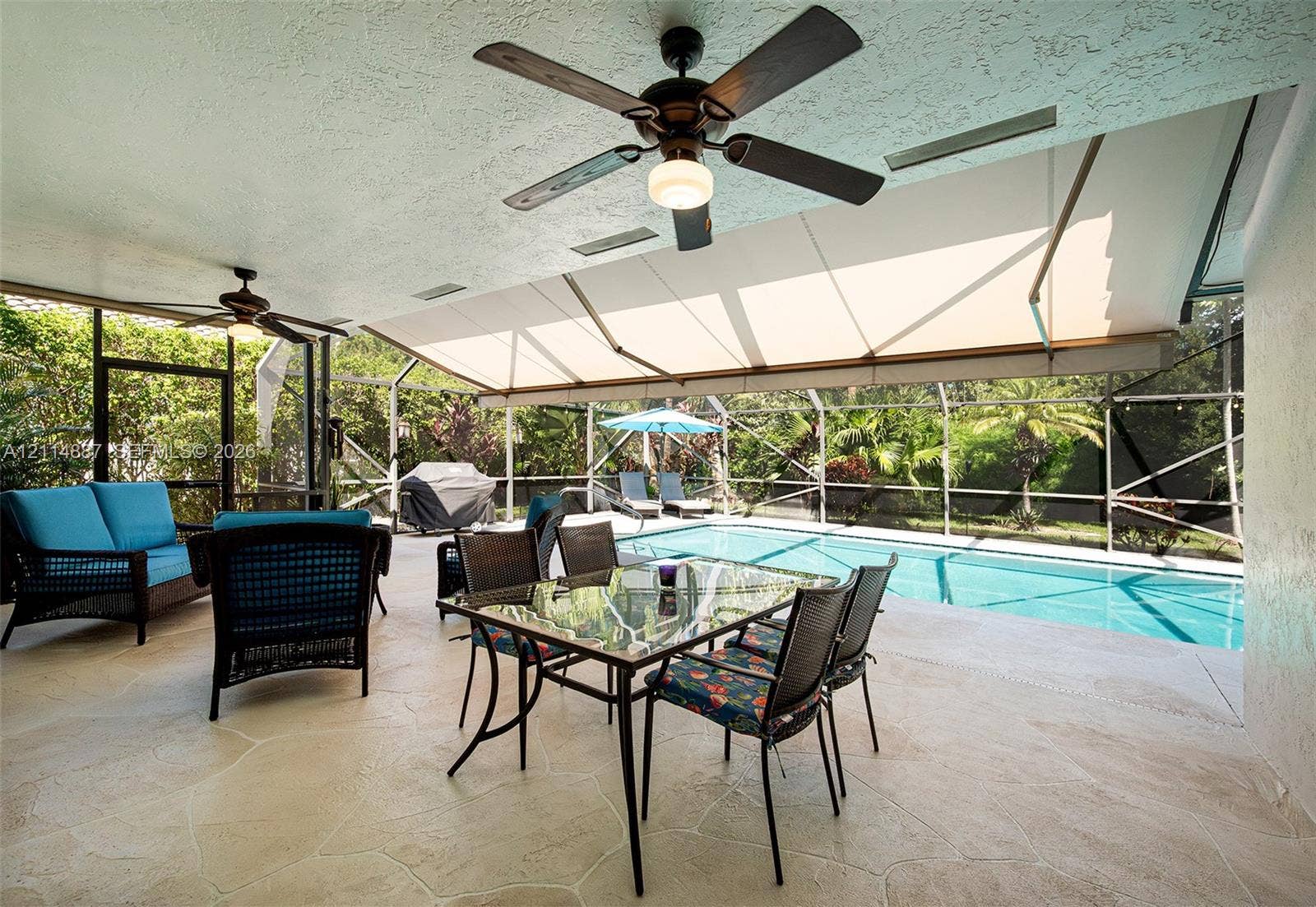 5722 Aspen Ridge Circle, Delray Beach, FL 33484 Covered outdoor patio featuring flagstone flooring, two ceiling fans, a retractable awning, and a screened enclosure surrounding the swimming pool