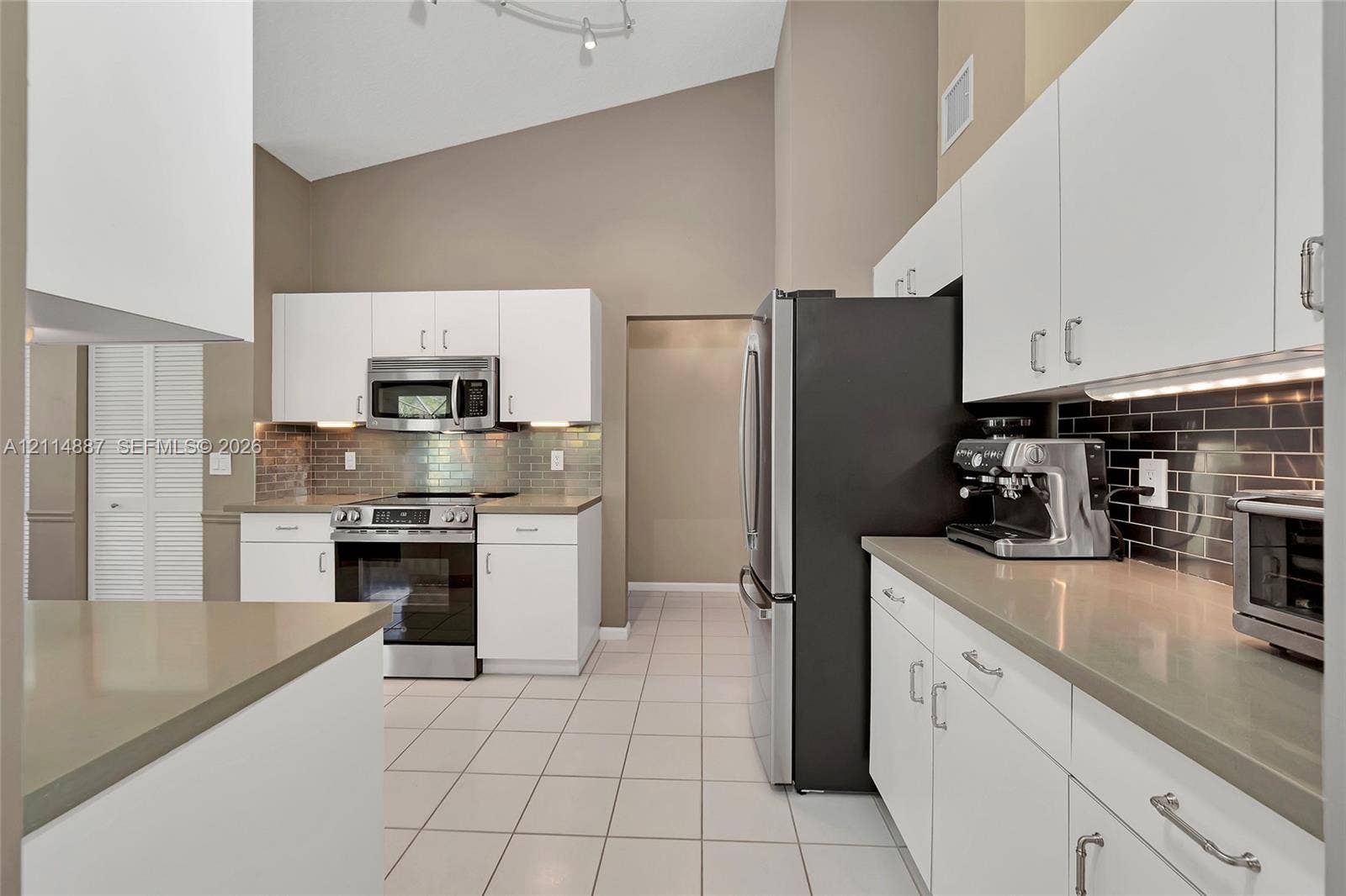 5722 Aspen Ridge Circle, Delray Beach, FL 33484 Kitchen featuring white cabinetry, solid surface countertops, stainless steel appliances, dark subway tile backsplash, and vaulted ceilings
