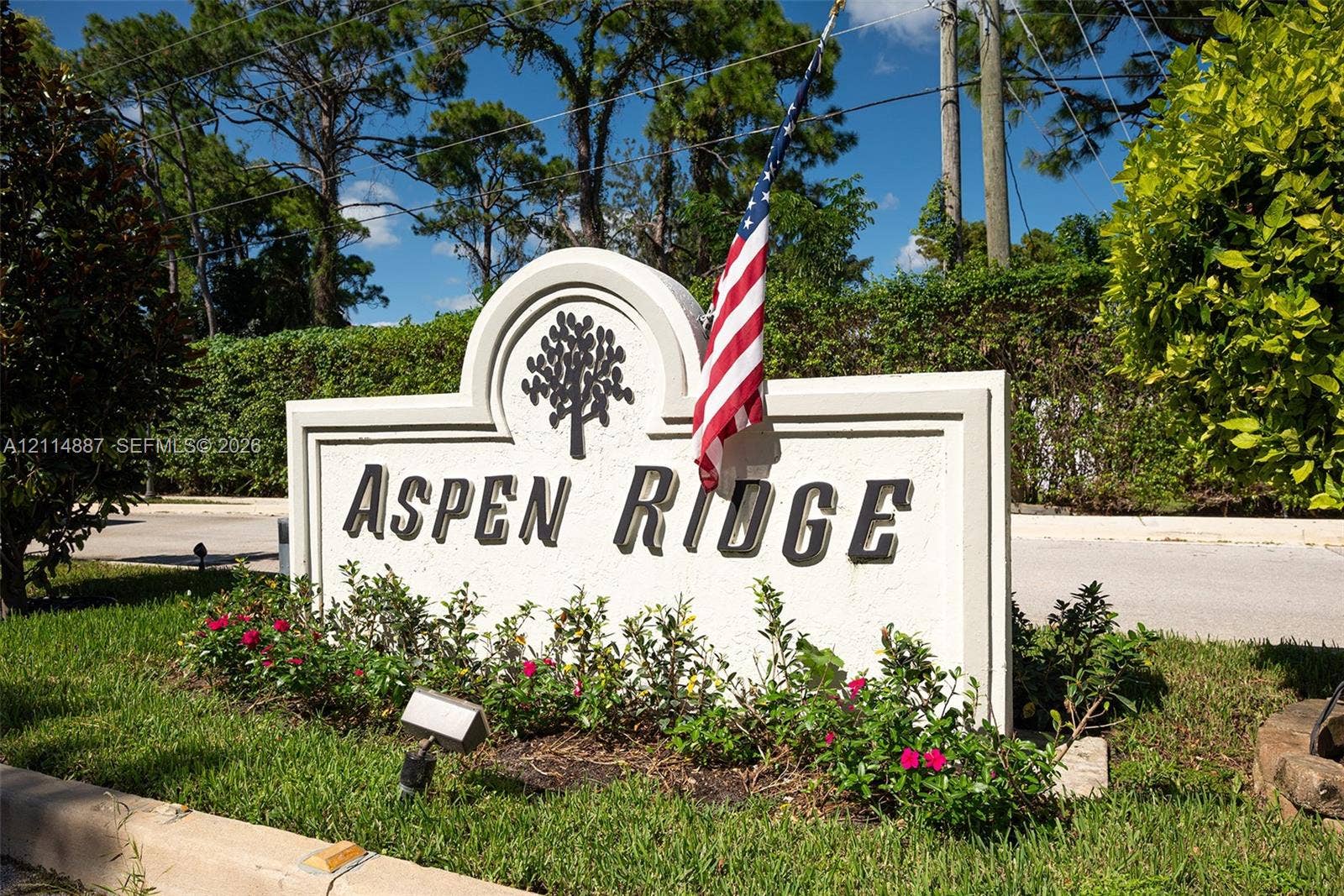 5722 Aspen Ridge Circle, Delray Beach, FL 33484 Custom monument signage featuring an arched profile, dimensional lettering, and integrated landscape beds with mature greenery and flowering shrubs
