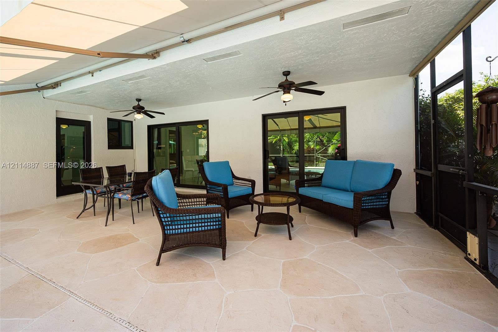 5722 Aspen Ridge Circle, Delray Beach, FL 33484 Covered patio featuring flagstone-style flooring, screen enclosure, dual ceiling fans, and sliding glass doors