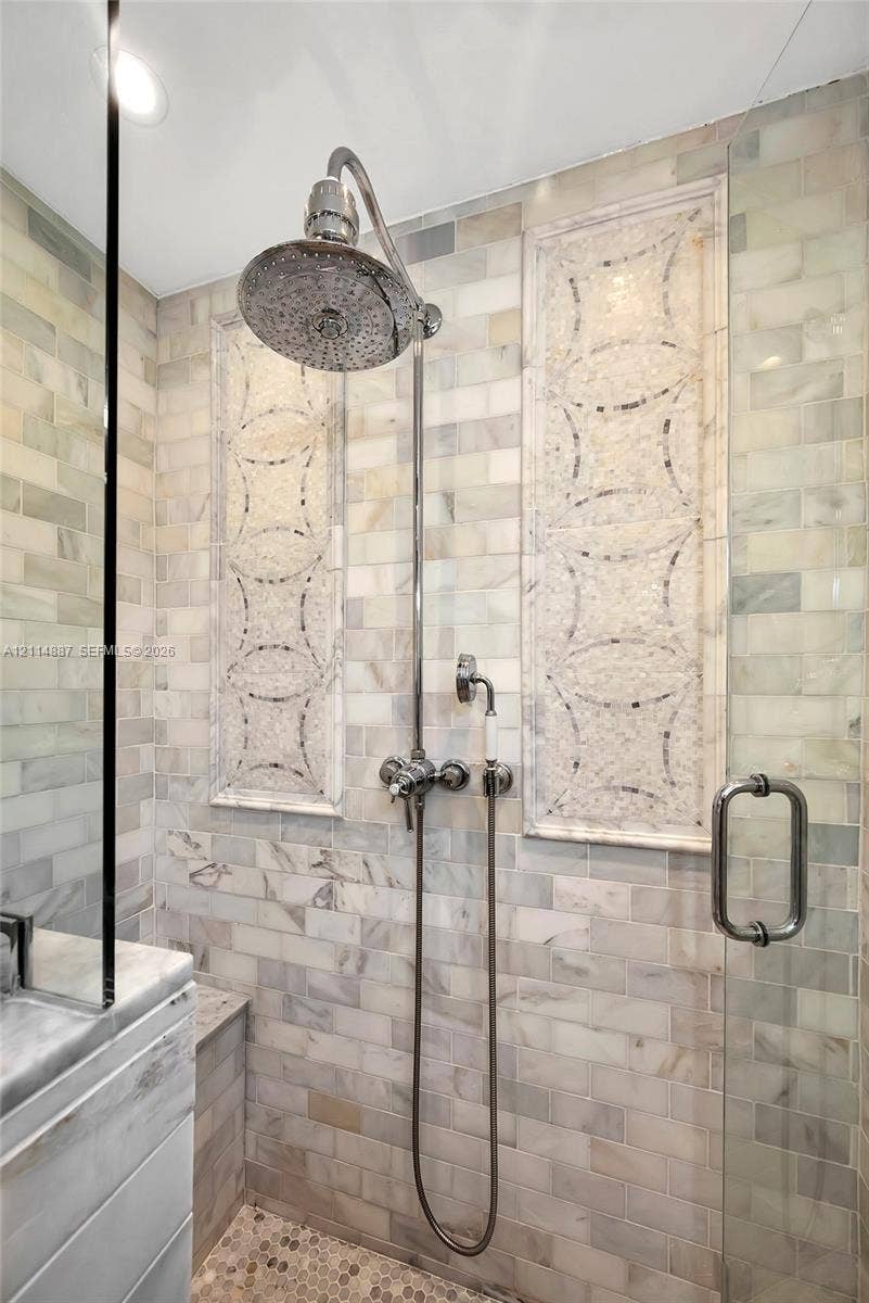 5722 Aspen Ridge Circle, Delray Beach, FL 33484 Walk-in shower featuring brick-pattern stone wall tile, decorative inset mosaic panels, pebble flooring, polished metal rainfall showerhead with handheld attachment, and a glass door enclosure