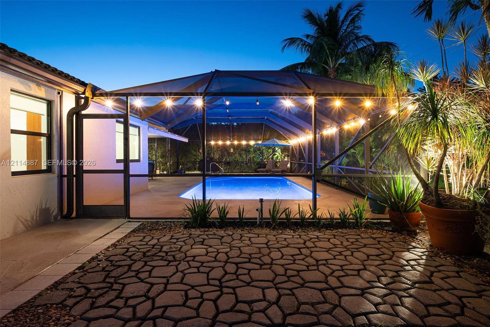 5722 Aspen Ridge Circle, Delray Beach, FL 33484 Screen-enclosed swimming pool with a paved deck, paver patio, and exterior string lighting