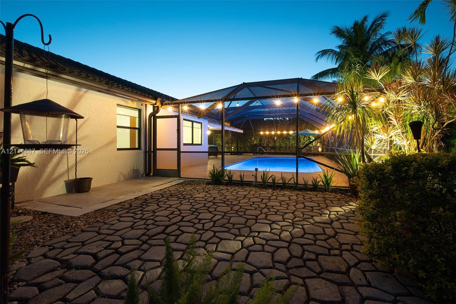 5722 Aspen Ridge Circle, Delray Beach, FL 33484 Screened-in outdoor pool area with stone-patterned paver patio, stucco exterior wall, and lush perimeter landscaping