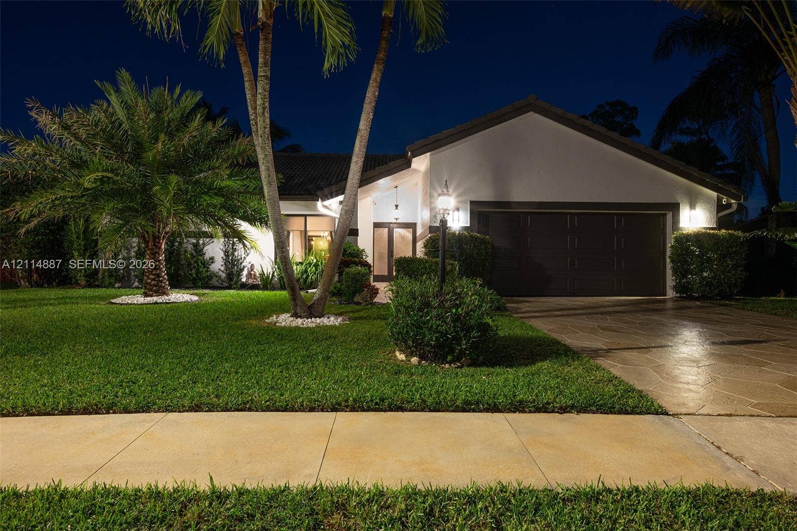 5722 Aspen Ridge Circle, Delray Beach, FL 33484 Single-story exterior featuring a stone-paver driveway, double-car garage, mature palm trees, and manicured landscaping