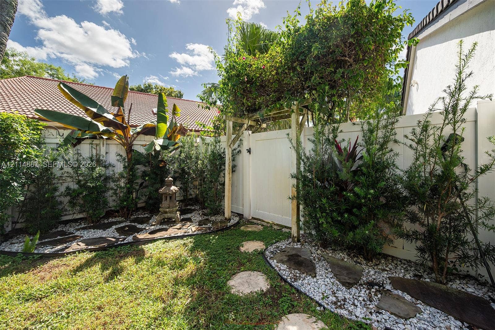 5722 Aspen Ridge Circle, Delray Beach, FL 33484 Enclosed backyard featuring white vinyl fencing, a decorative wooden arbor, stone paver pathways, and landscape plantings