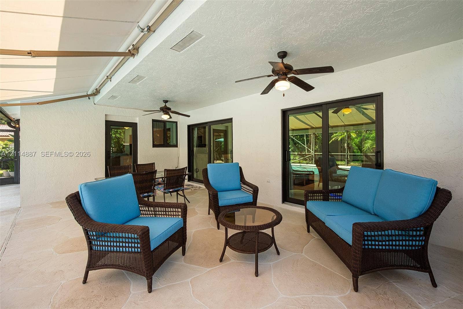 5722 Aspen Ridge Circle, Delray Beach, FL 33484 Covered patio featuring flagstone-style flooring, dual ceiling fans, a retractable exterior awning, and sliding glass doors