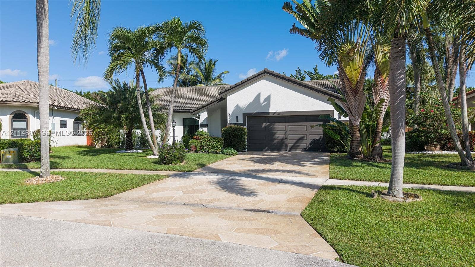 5722 Aspen Ridge Circle, Delray Beach, FL 33484 Stucco exterior with a multi-car garage, stone-paver driveway, and mature palm landscaping