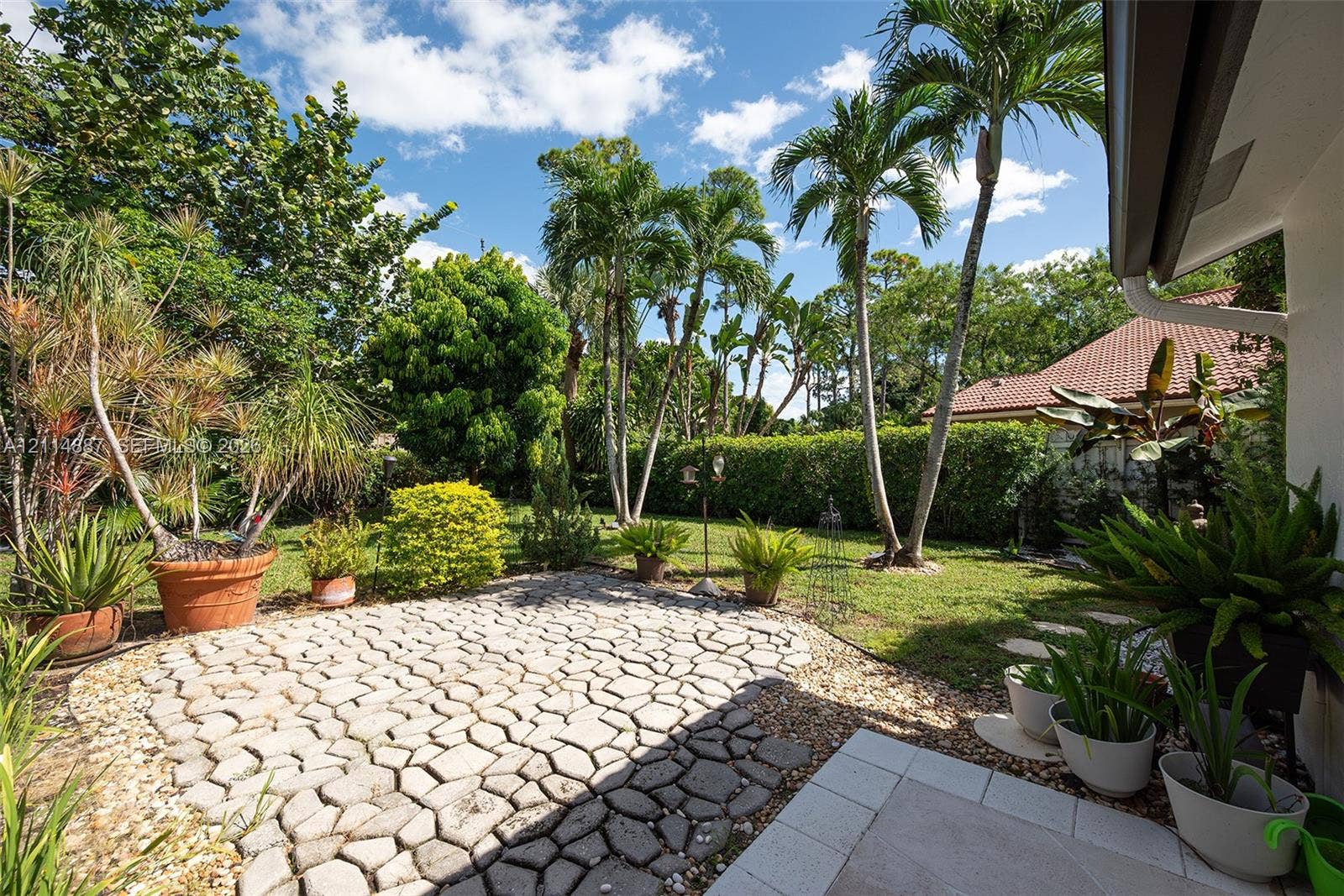 5722 Aspen Ridge Circle, Delray Beach, FL 33484 Landscaped backyard featuring a paved stone patio, manicured lawn, established palm trees, and perimeter shrubbery