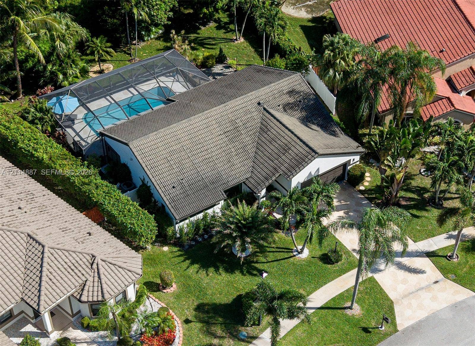 5722 Aspen Ridge Circle, Delray Beach, FL 33484 Aerial perspective of a residence featuring a screen-enclosed pool, tile roofing, a paved driveway, and mature palm landscaping