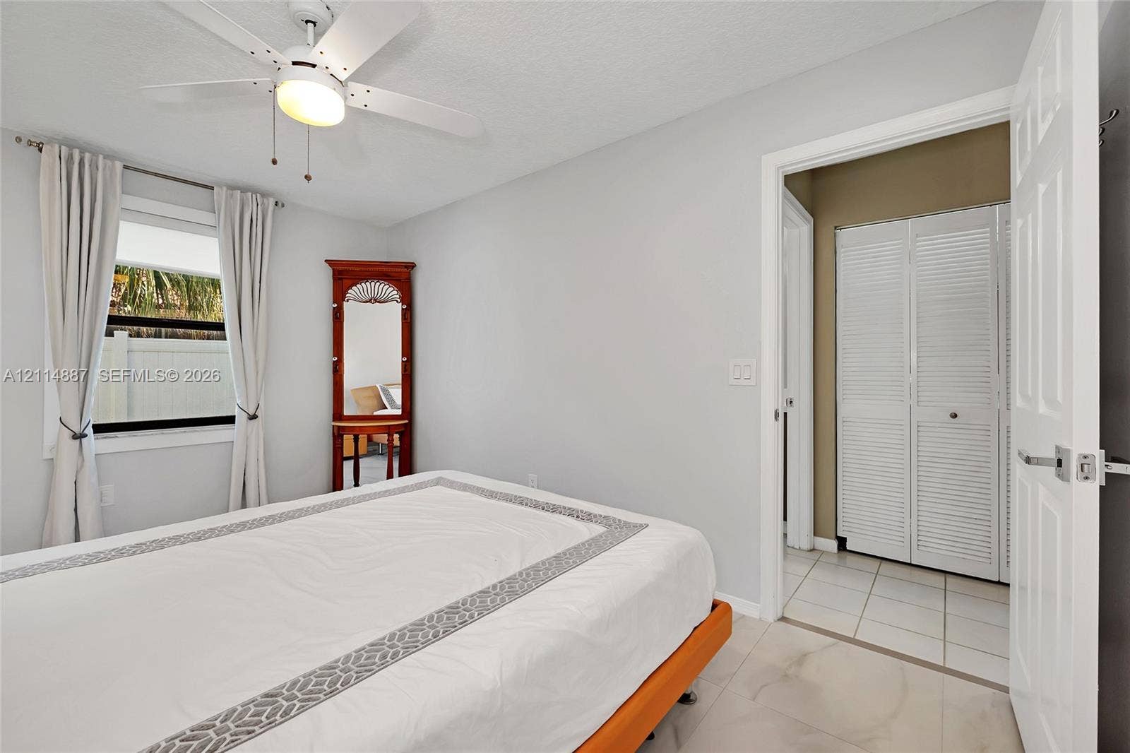 5722 Aspen Ridge Circle, Delray Beach, FL 33484 Neutral-toned interior featuring large-format tile flooring, white bi-fold closet doors, and a ceiling-mounted light fixture with a multi-blade fan