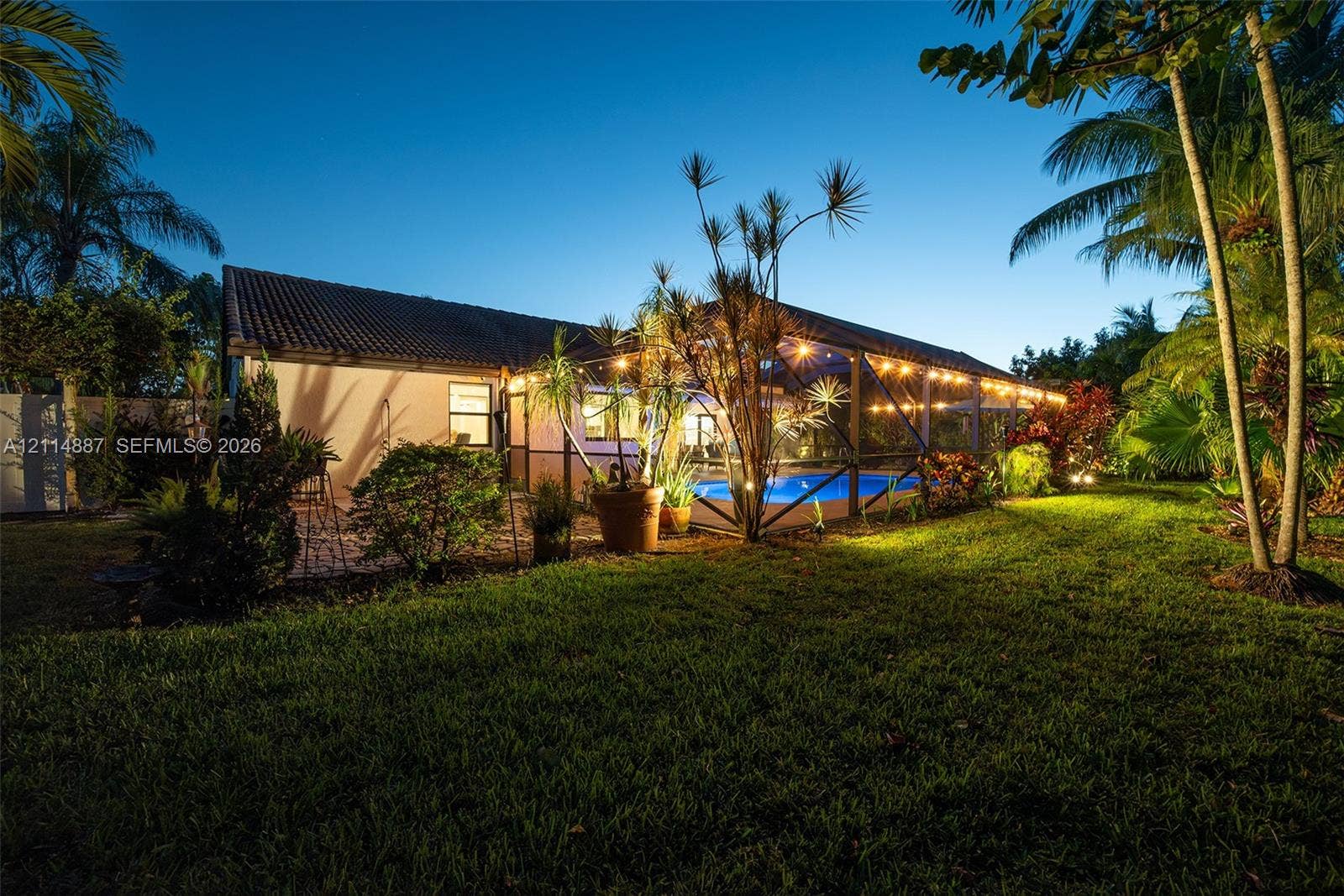 5722 Aspen Ridge Circle, Delray Beach, FL 33484 Backyard featuring a screened-in pool enclosure, paver patio, established landscaping, and palm trees