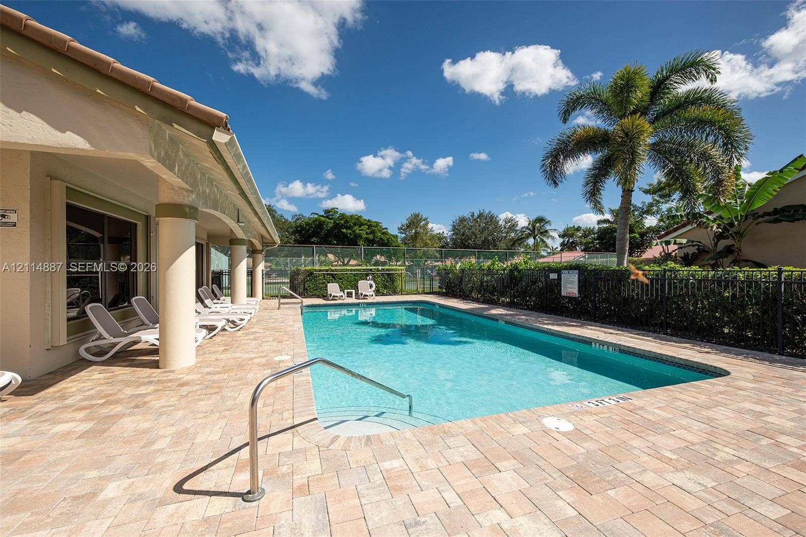 5722 Aspen Ridge Circle, Delray Beach, FL 33484 Outdoor swimming pool featuring a brick paver deck, covered patio with structural columns, and perimeter metal fencing