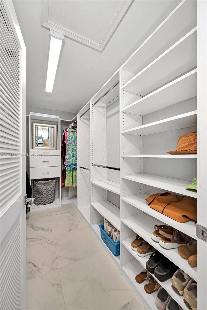 5722 Aspen Ridge Circle, Delray Beach, FL 33484 Walk-in closet featuring floor-to-ceiling white built-in shelving, integrated dresser drawers, metal hanging rods, and large-format tile flooring