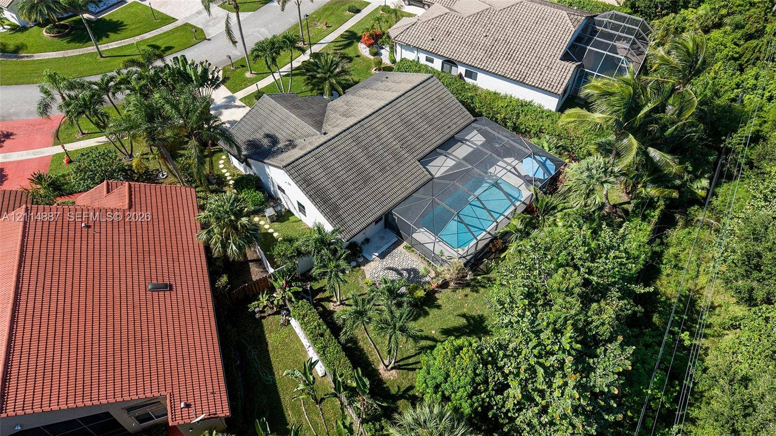 5722 Aspen Ridge Circle, Delray Beach, FL 33484 Aerial perspective of a property featuring a screened-in swimming pool, paved patio, lush landscaping, and mature palm trees