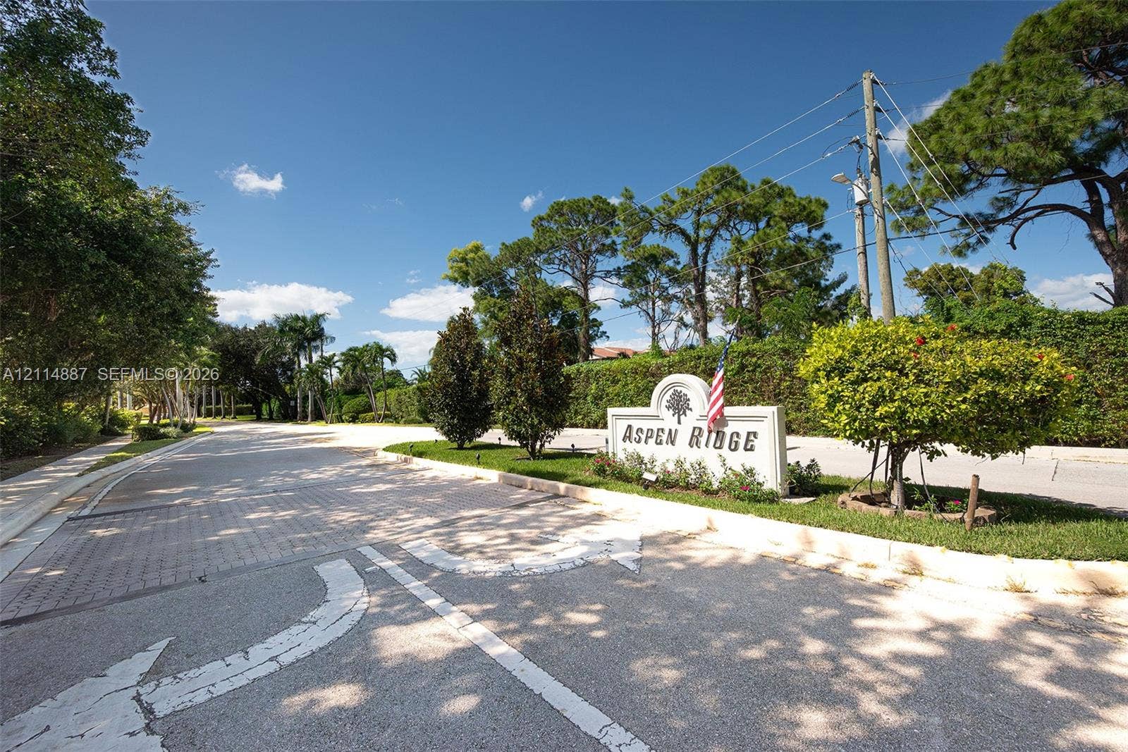 5722 Aspen Ridge Circle, Delray Beach, FL 33484 Community entrance featuring stone-paver roadway, landscaped grounds, mature pine and palm trees, and a monument sign
