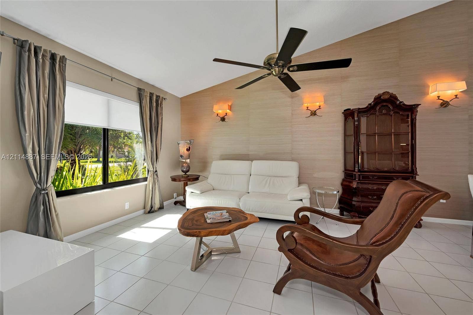 5722 Aspen Ridge Circle, Delray Beach, FL 33484 Vaulted ceiling with a central multi-blade ceiling fan, textured accent wall, polished tile flooring, and wall-mounted sconce lighting