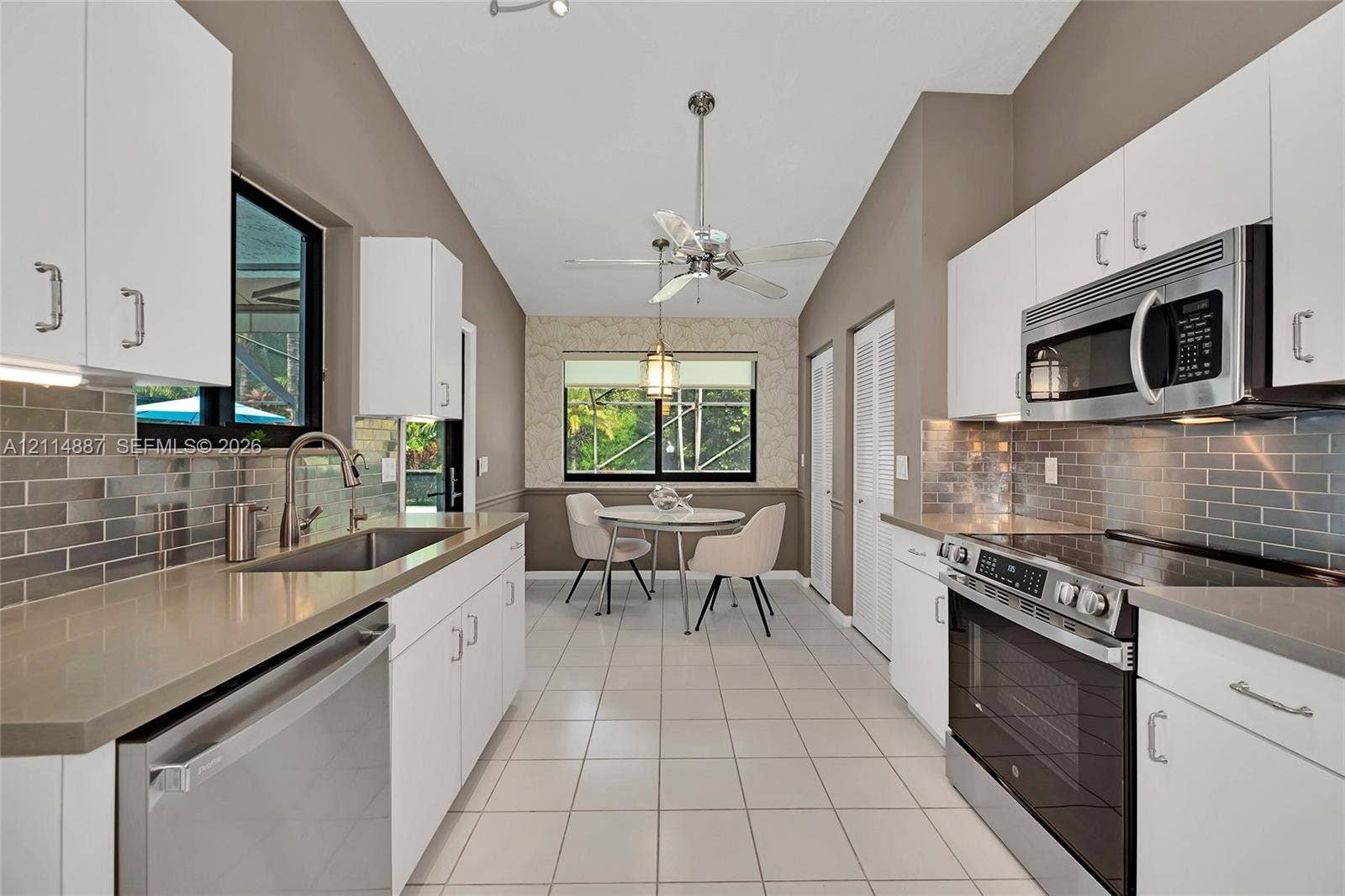 5722 Aspen Ridge Circle, Delray Beach, FL 33484 Kitchen featuring white shaker-style cabinetry, quartz countertops, stainless steel appliances, subway tile backsplash, and vaulted ceilings