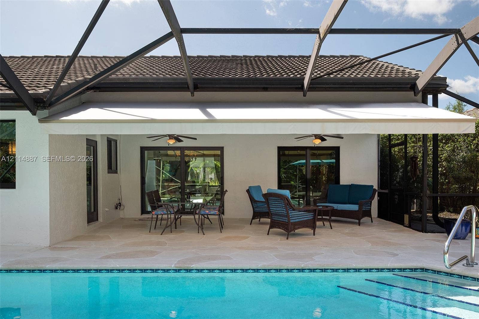 5722 Aspen Ridge Circle, Delray Beach, FL 33484 Covered patio featuring natural stone pavers, a retractable awning, dual ceiling fans, and a screened enclosure overlooking a swimming pool