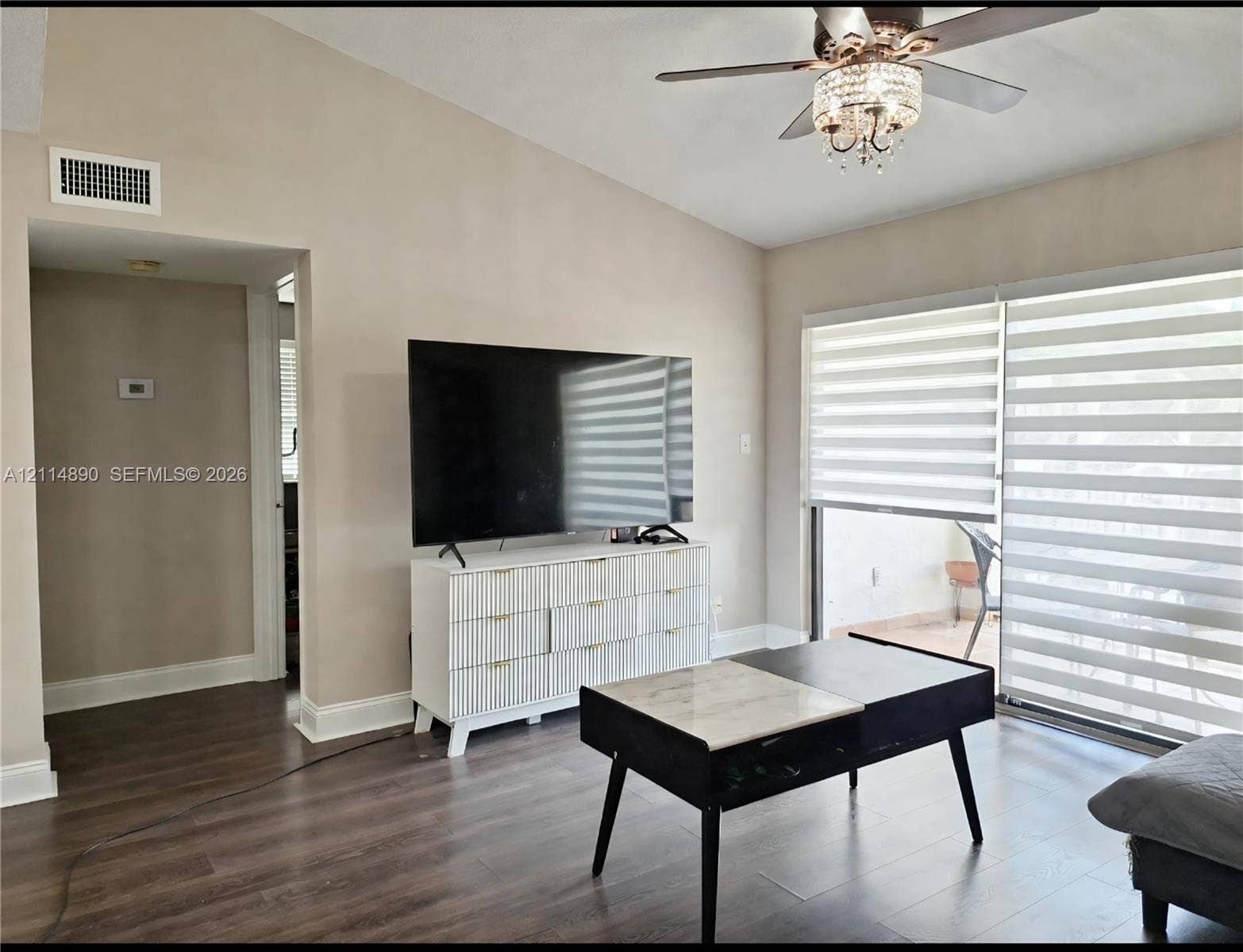 610 S Park Road, #28-1, Hollywood, FL 33021 Vaulted ceiling featuring a central ceiling fan with integrated crystal chandelier, wood-finish flooring, and sliding glass doors with roller shades
