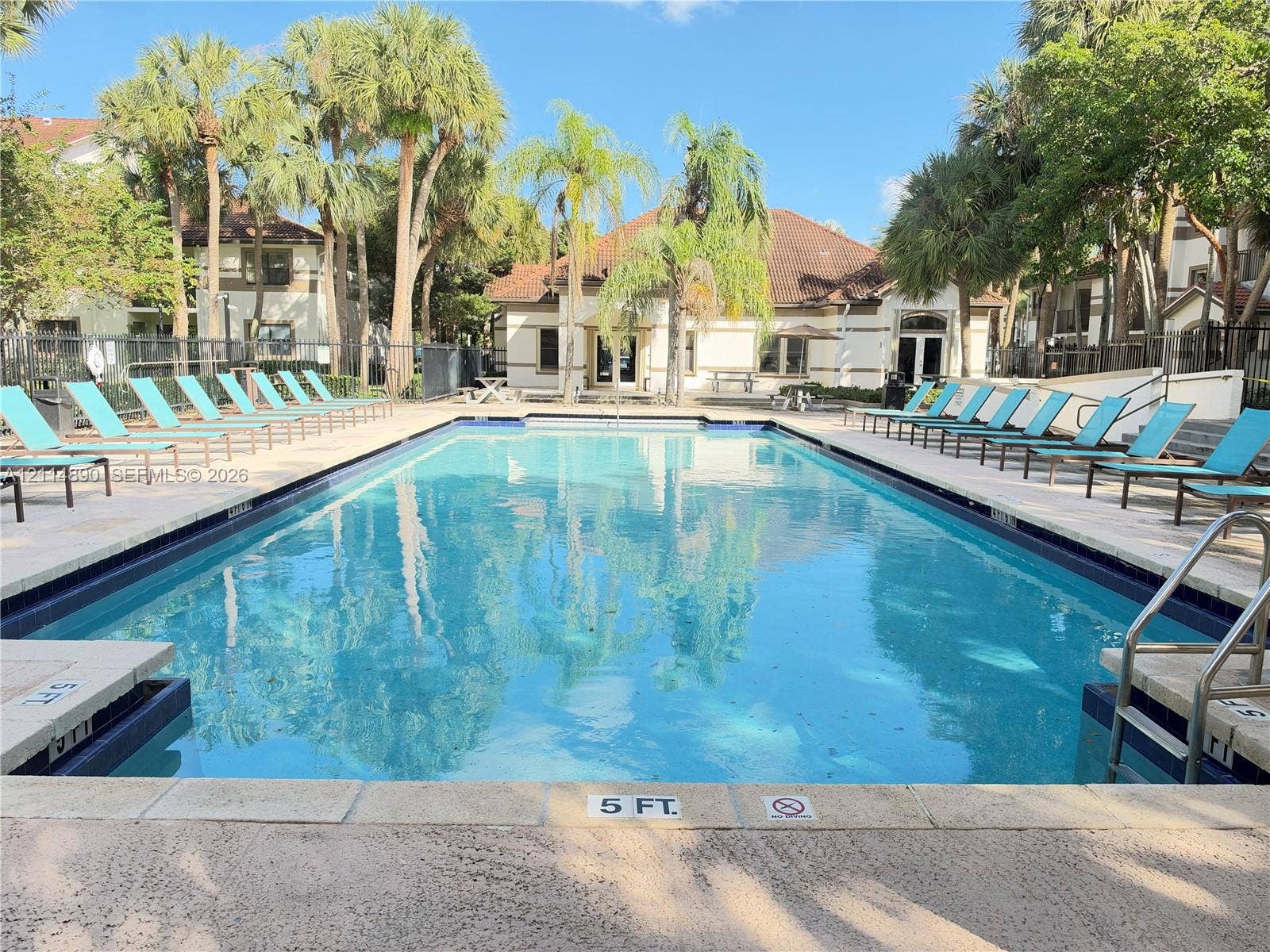 610 S Park Road, #28-1, Hollywood, FL 33021 Swimming pool with a paved deck, metal handrail, and perimeter landscaping featuring mature palm trees