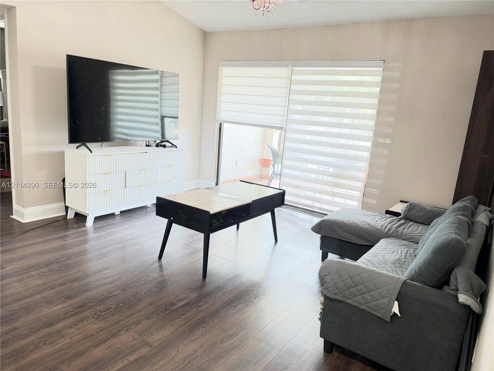 610 S Park Road, #28-1, Hollywood, FL 33021 Vaulted ceiling with a central pendant light fixture, dark wood-finish flooring, and large sliding glass doors featuring horizontal banded shades