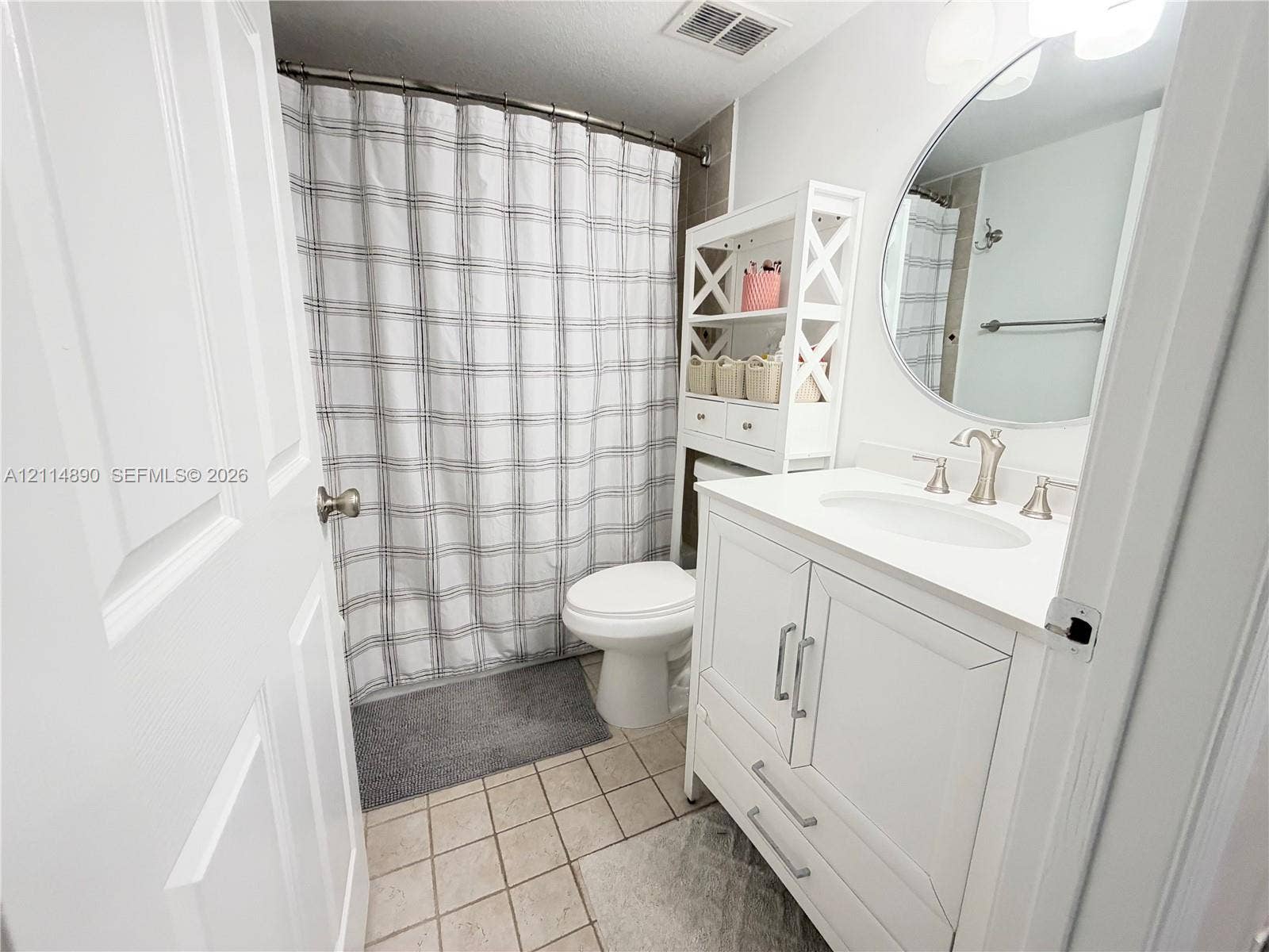 610 S Park Road, #28-1, Hollywood, FL 33021 White vanity cabinet with a stone-composite countertop, undermount sink, brushed nickel faucet, and circular wall mirror with integrated lighting