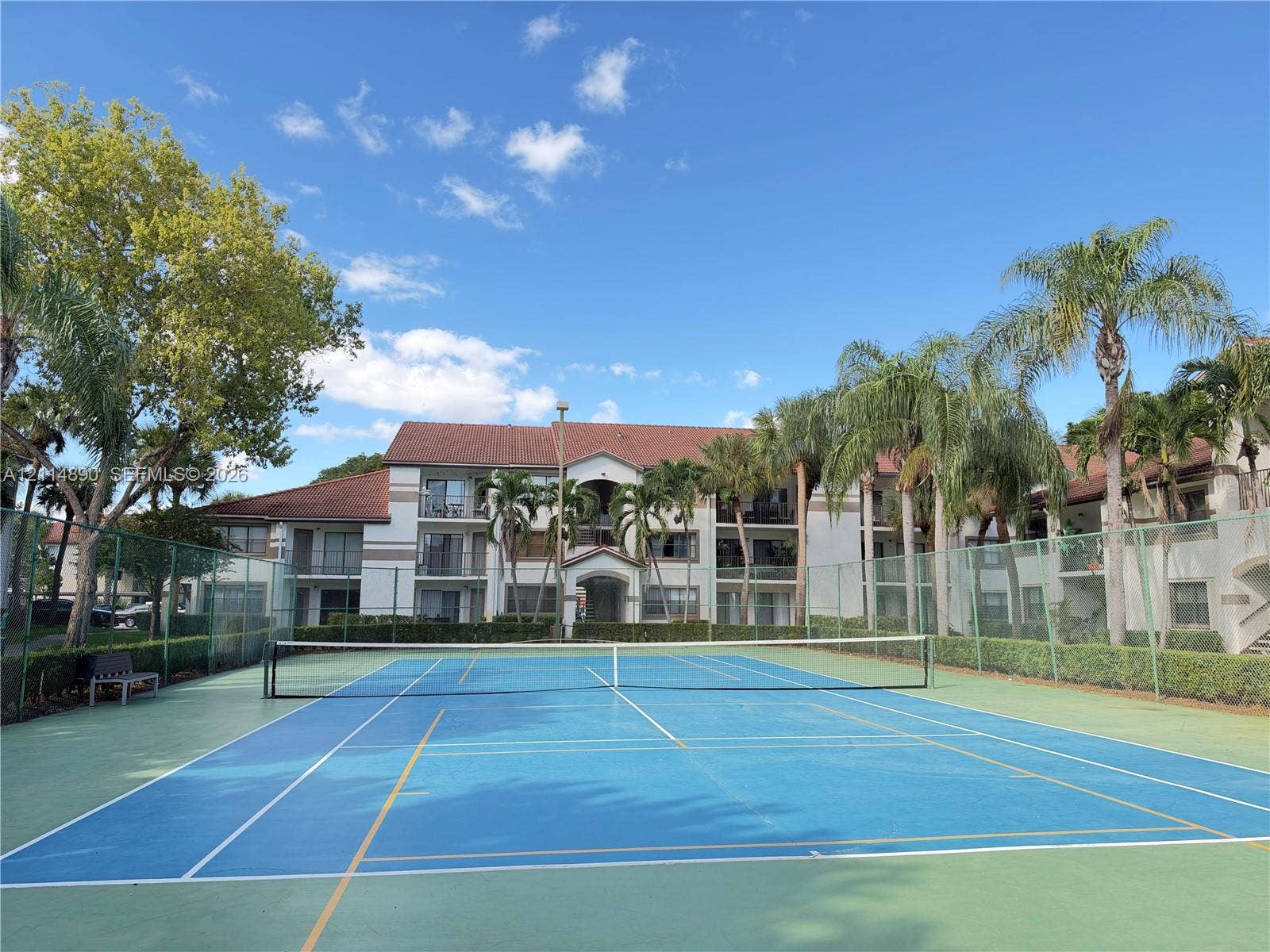 610 S Park Road, #28-1, Hollywood, FL 33021 Hard-surface tennis court enclosed by perimeter fencing and landscaped borders, featuring multi-story residential architecture with terracotta-style roof tiling
