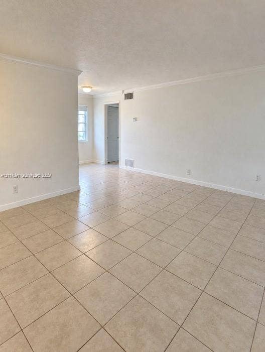 Neutral interior space featuring large-format ceramic tile flooring, crown molding, and smooth-finish walls