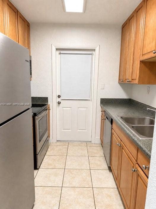 Kitchen featuring wood cabinetry, stone-finish countertops, stainless steel appliances, double-basin sink, and tile flooring