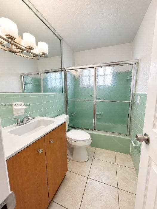 Bathroom featuring a wood-finish vanity with a rectangular sink, full-width mirror, tile surround tub-shower with sliding glass doors, and tile flooring