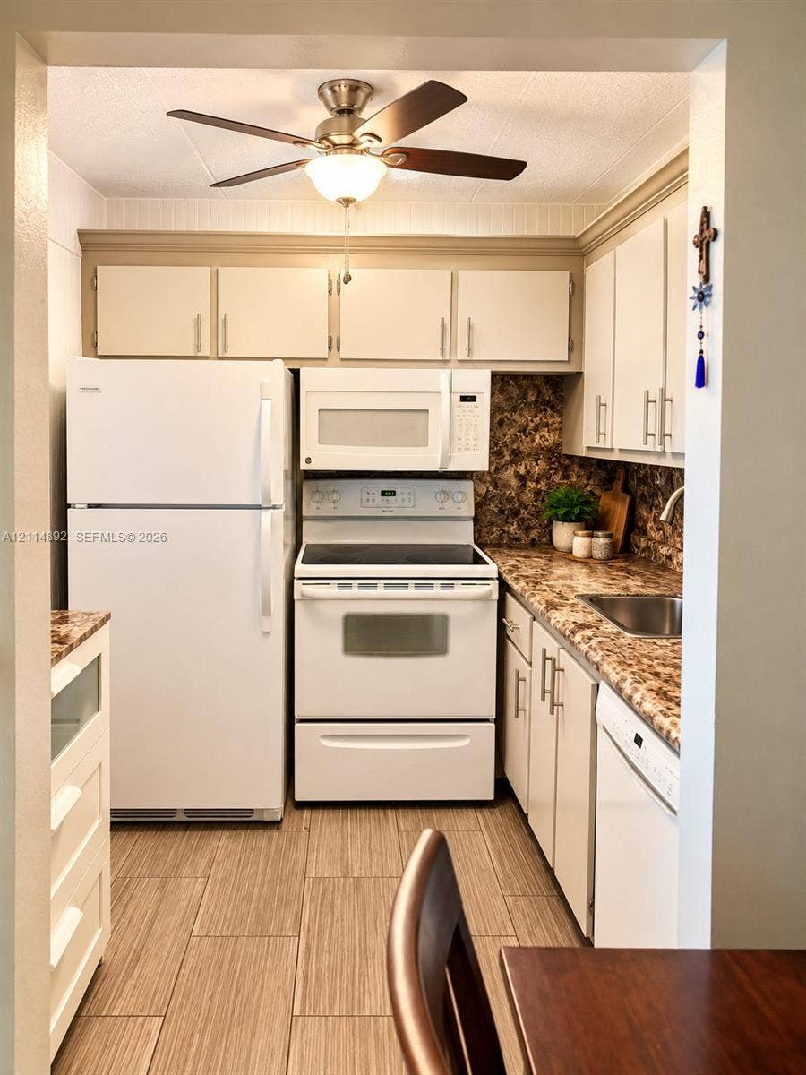 582 Durham U, #582, Deerfield Beach, FL 33442 Kitchen featuring white cabinetry with metallic pulls, patterned laminate countertops, a stainless steel sink, wood-finish tile flooring, and a ceiling-mounted fan with integrated lighting