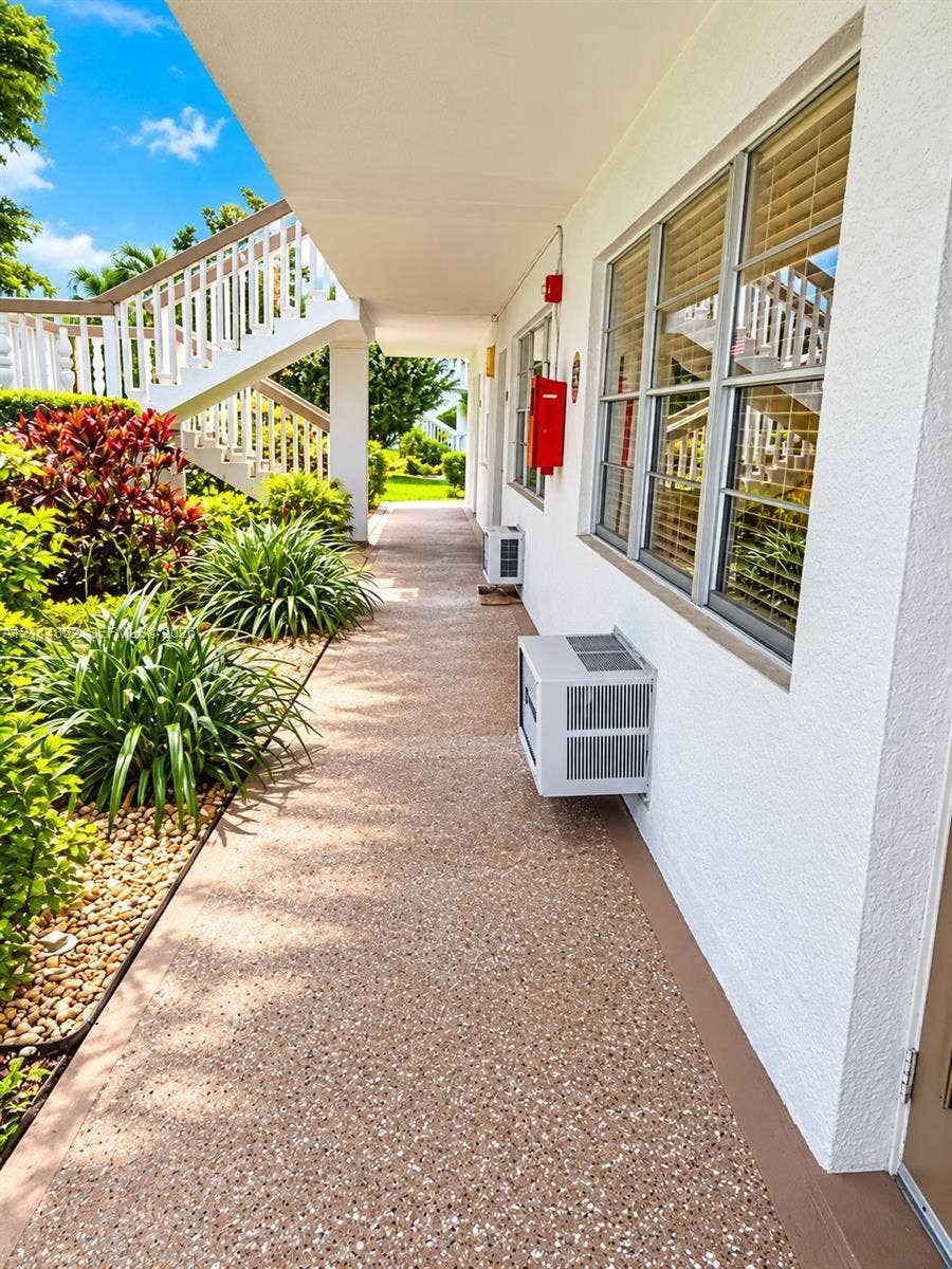 582 Durham U, #582, Deerfield Beach, FL 33442 Exterior walkway featuring a pebble-finish surface, white stucco facade, multi-pane windows with integrated blinds, and built-in metal staircase railings