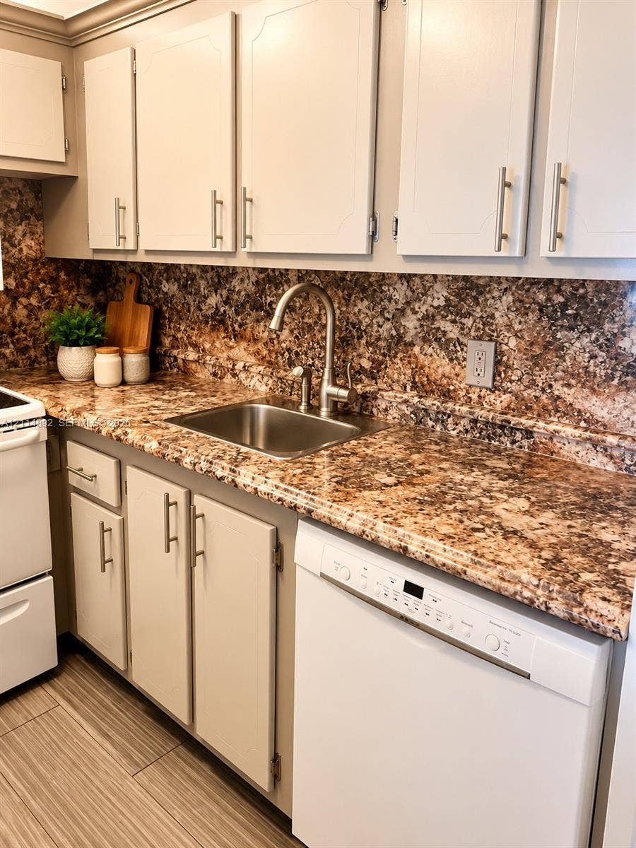 582 Durham U, #582, Deerfield Beach, FL 33442 Kitchen featuring white cabinetry with brushed metal hardware, stone-patterned countertops, matching full-height stone-patterned backsplash, stainless steel sink with high-arc faucet, and wood-finish tile flooring