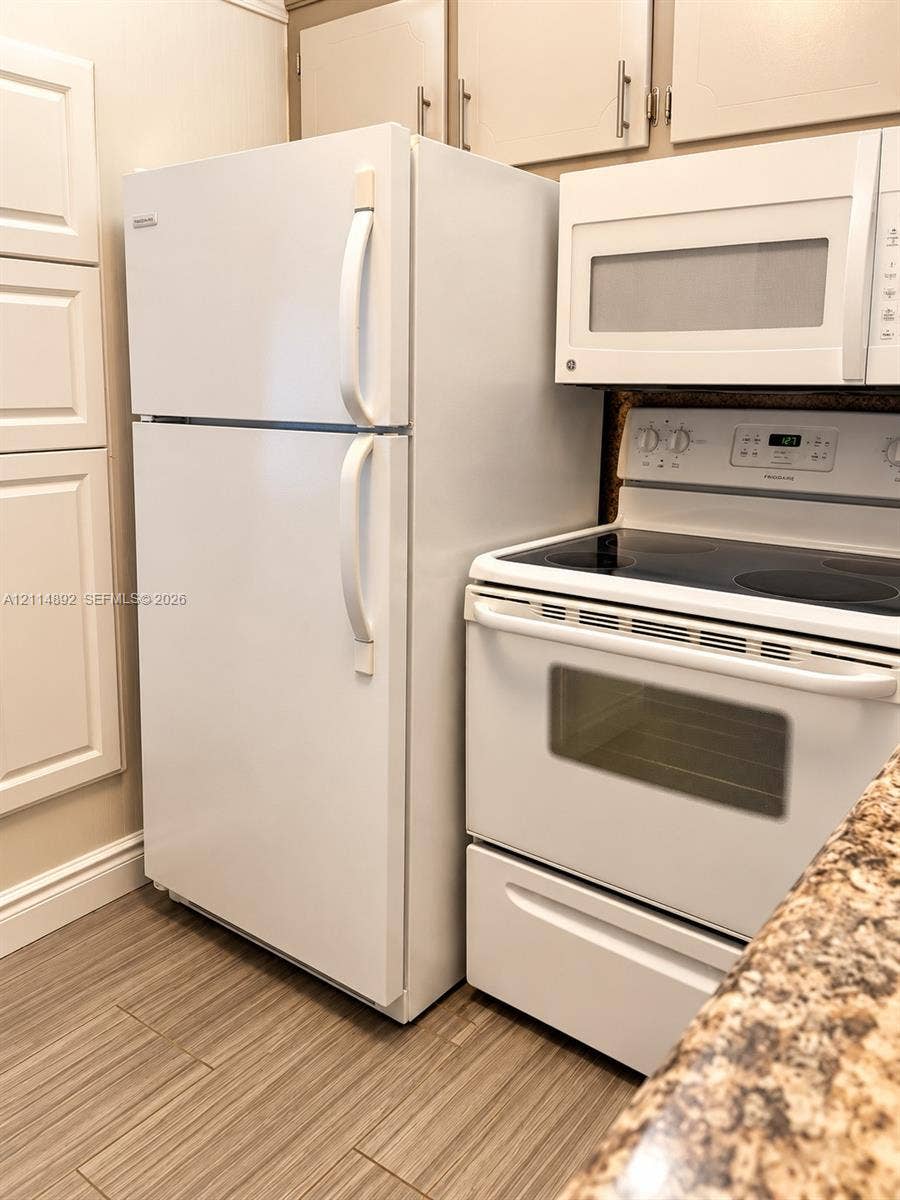 582 Durham U, #582, Deerfield Beach, FL 33442 Kitchen featuring white upper cabinetry, a top-freezer refrigerator, over-the-range microwave, electric smooth-top range, and stone-finish countertops