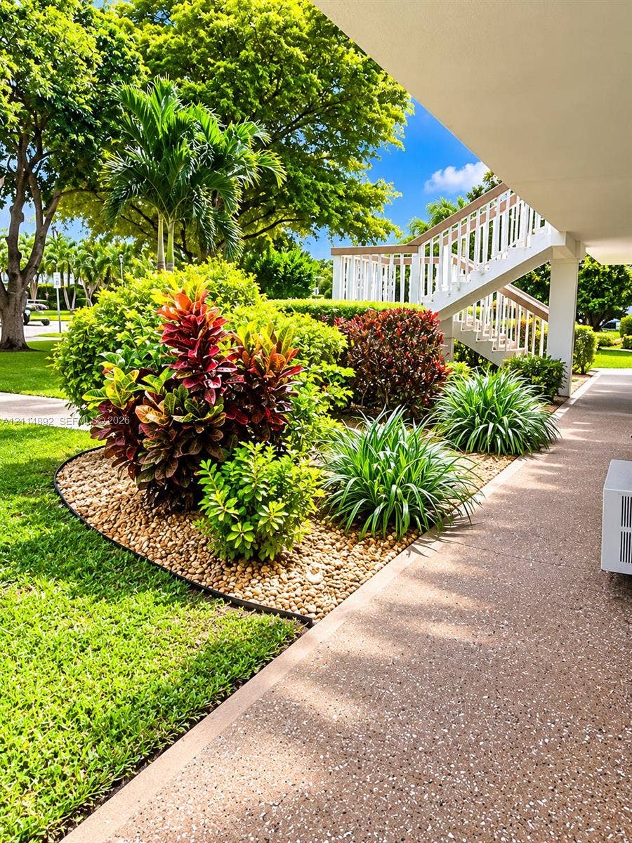 582 Durham U, #582, Deerfield Beach, FL 33442 Landscaped garden featuring mature trees, colorful foliage, and decorative stone ground cover with concrete walkway and external staircase